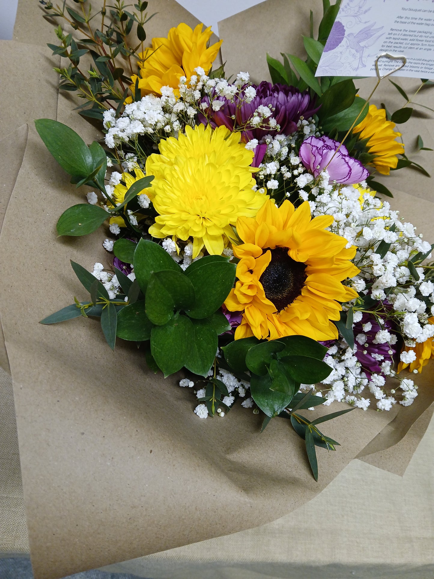 Bouquet of sunflowers, purple flowers, and greenery on brown paper